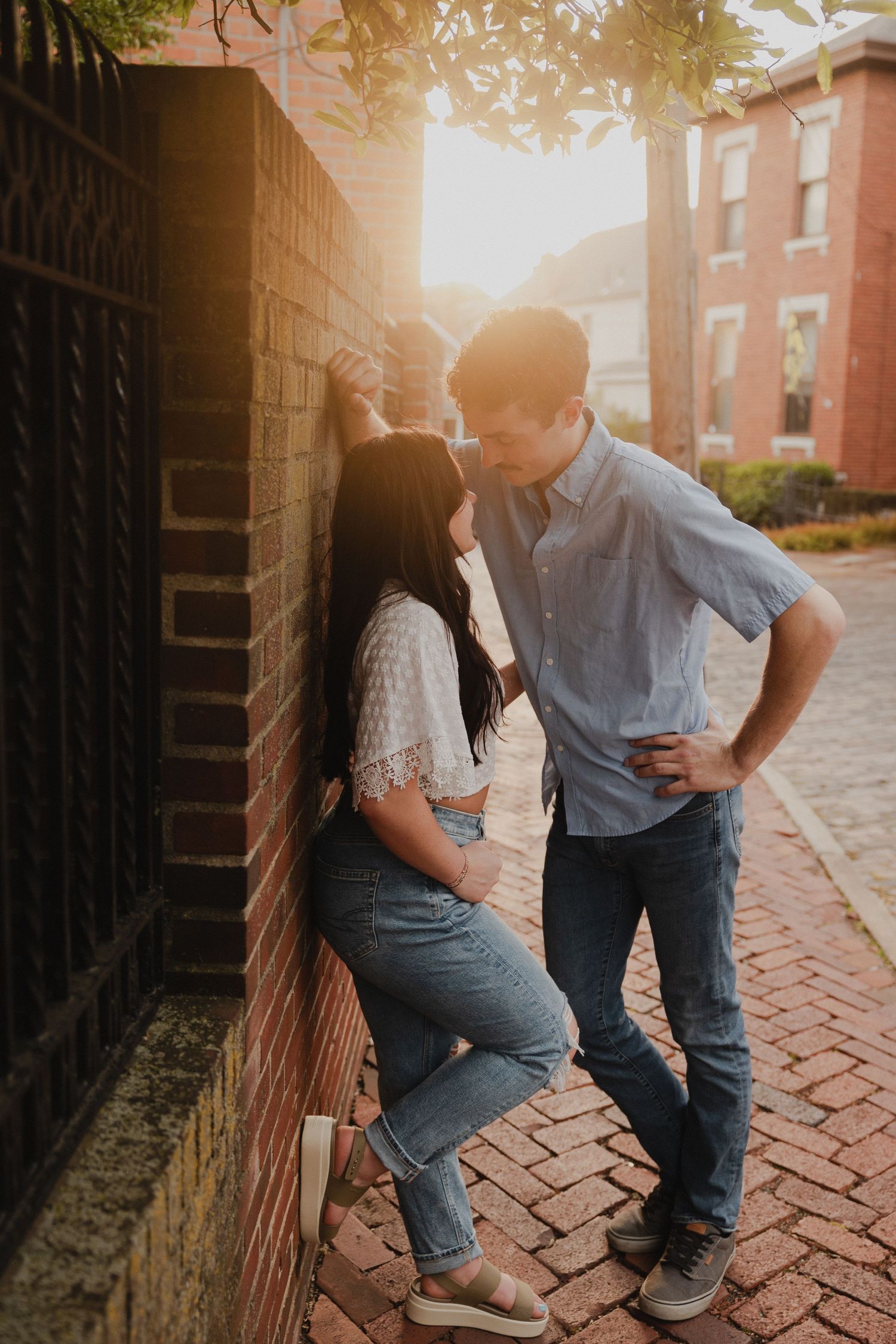 Intimate moment between couple against brick wall on cobblestone street at sunset.