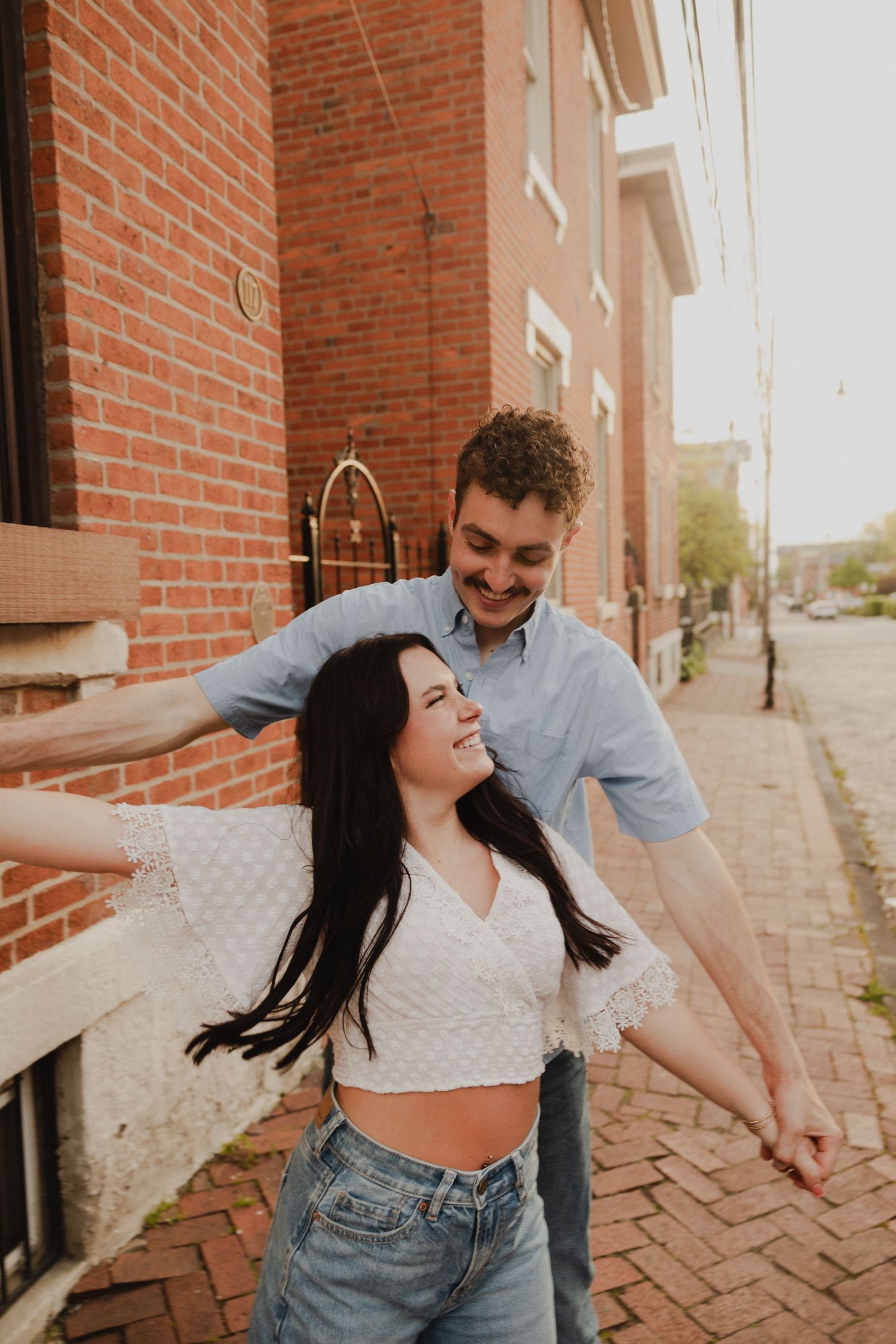 Joyful moment captured between couple on brick sidewalk during sunset photoshoot.
