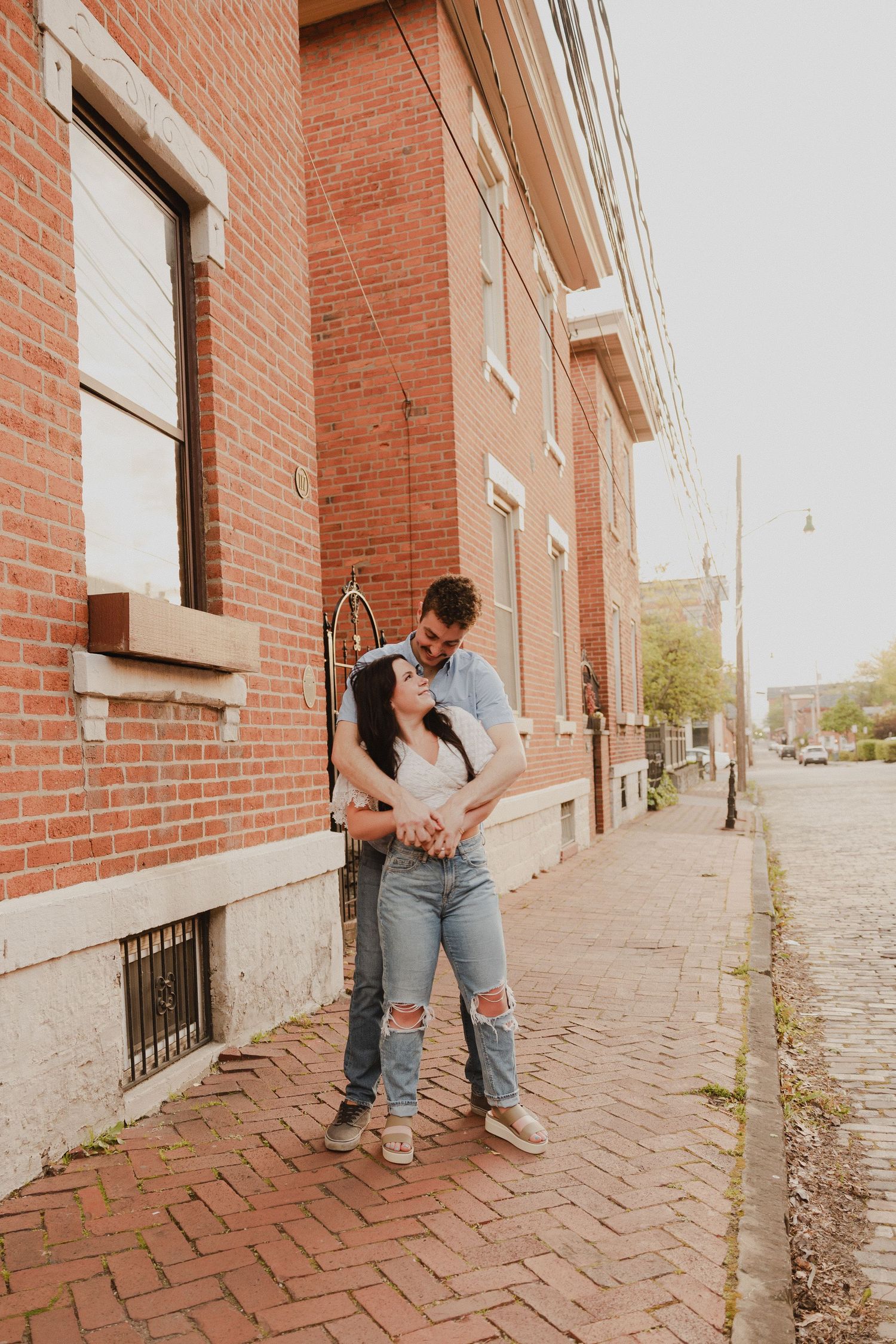 Romantic pose on historic brick sidewalk with traditional architecture in background.