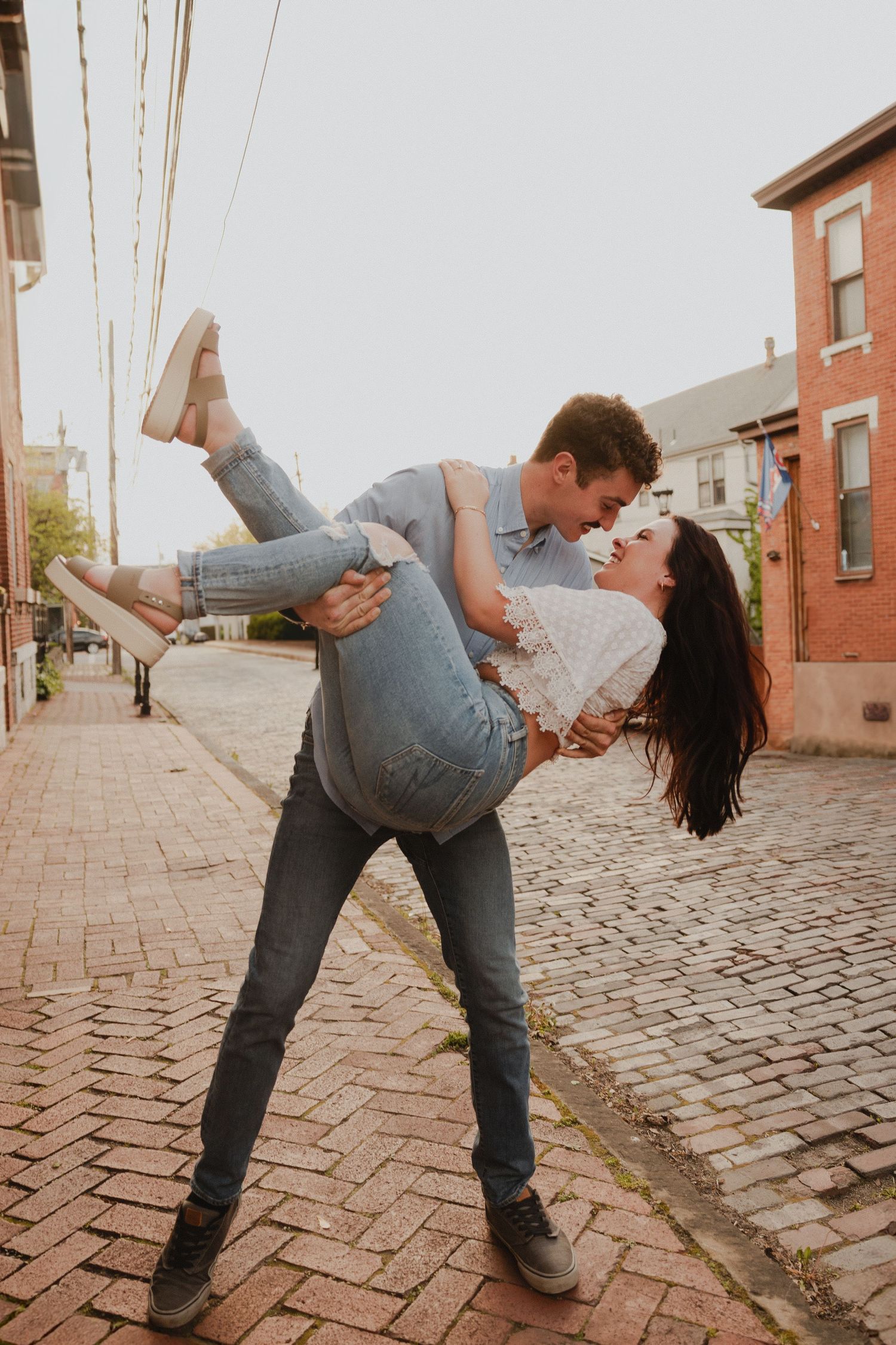A romantic couple shares a playful dance dip on a brick sidewalk in front of historic buildings.