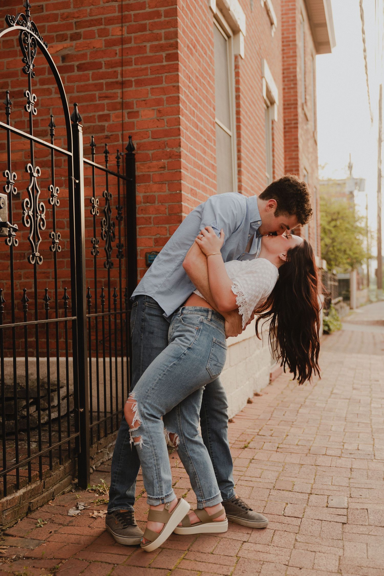 Couple sharing an intimate moment against an ornate iron gate and brick wall backdrop.