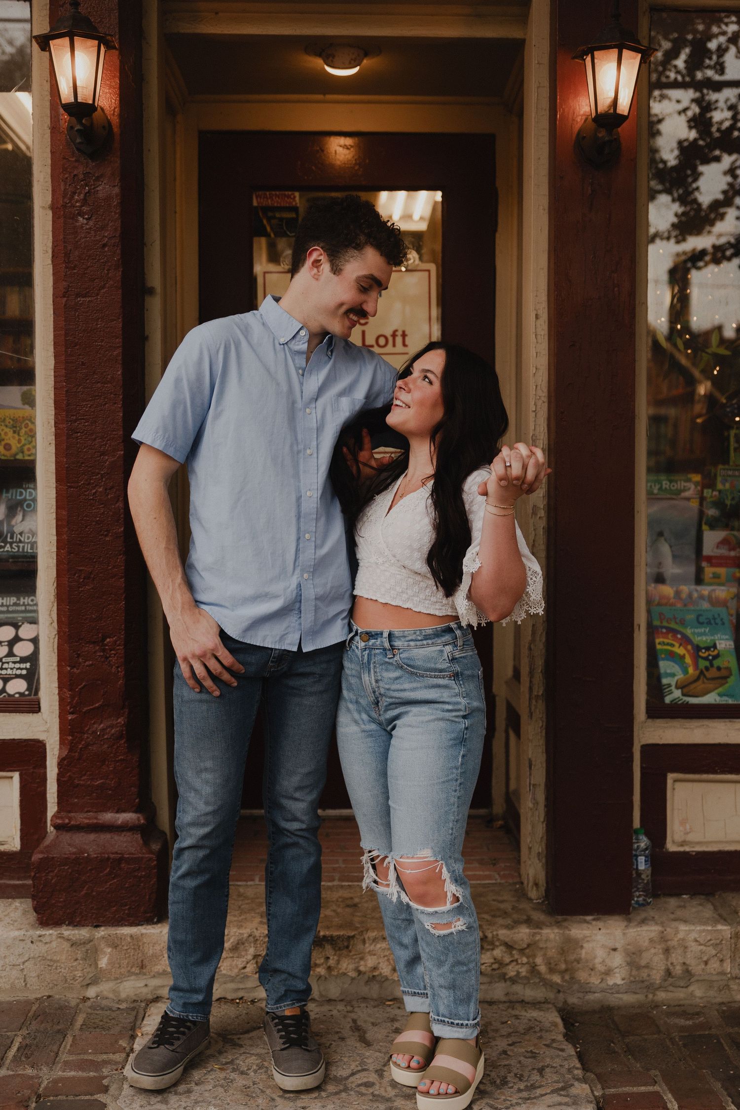 A couple stands together in a doorway with warm lighting and lanterns.