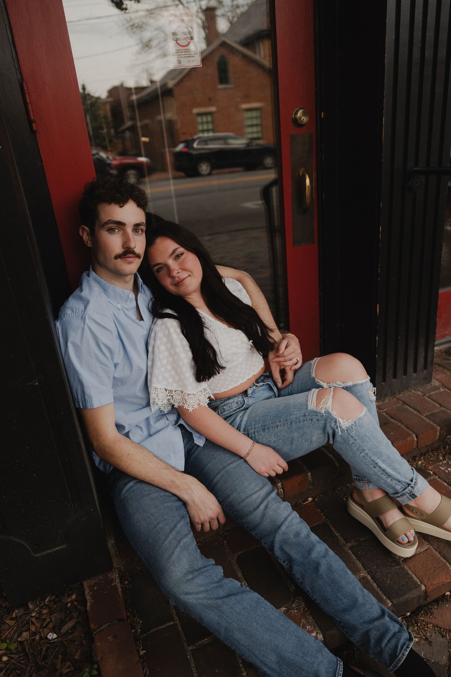 A couple sits relaxing on brick steps in front of a doorway.