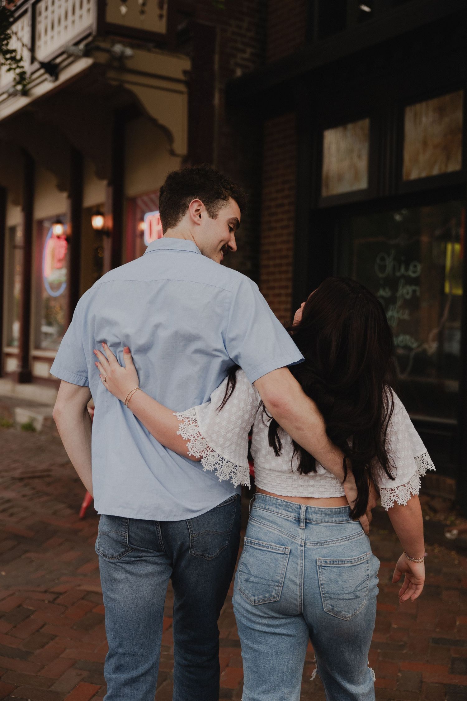 A couple walks together down a brick sidewalk in a historic downtown area.