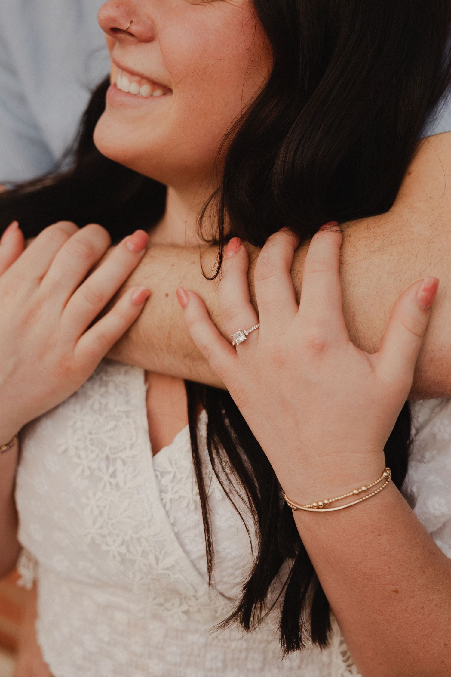 Close-up of hands with engagement ring against white lace top and dark hair.