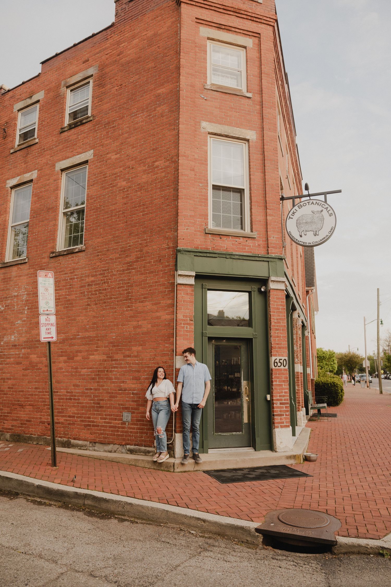 Couple stands outside historic brick building with green doorway on cobblestone street.