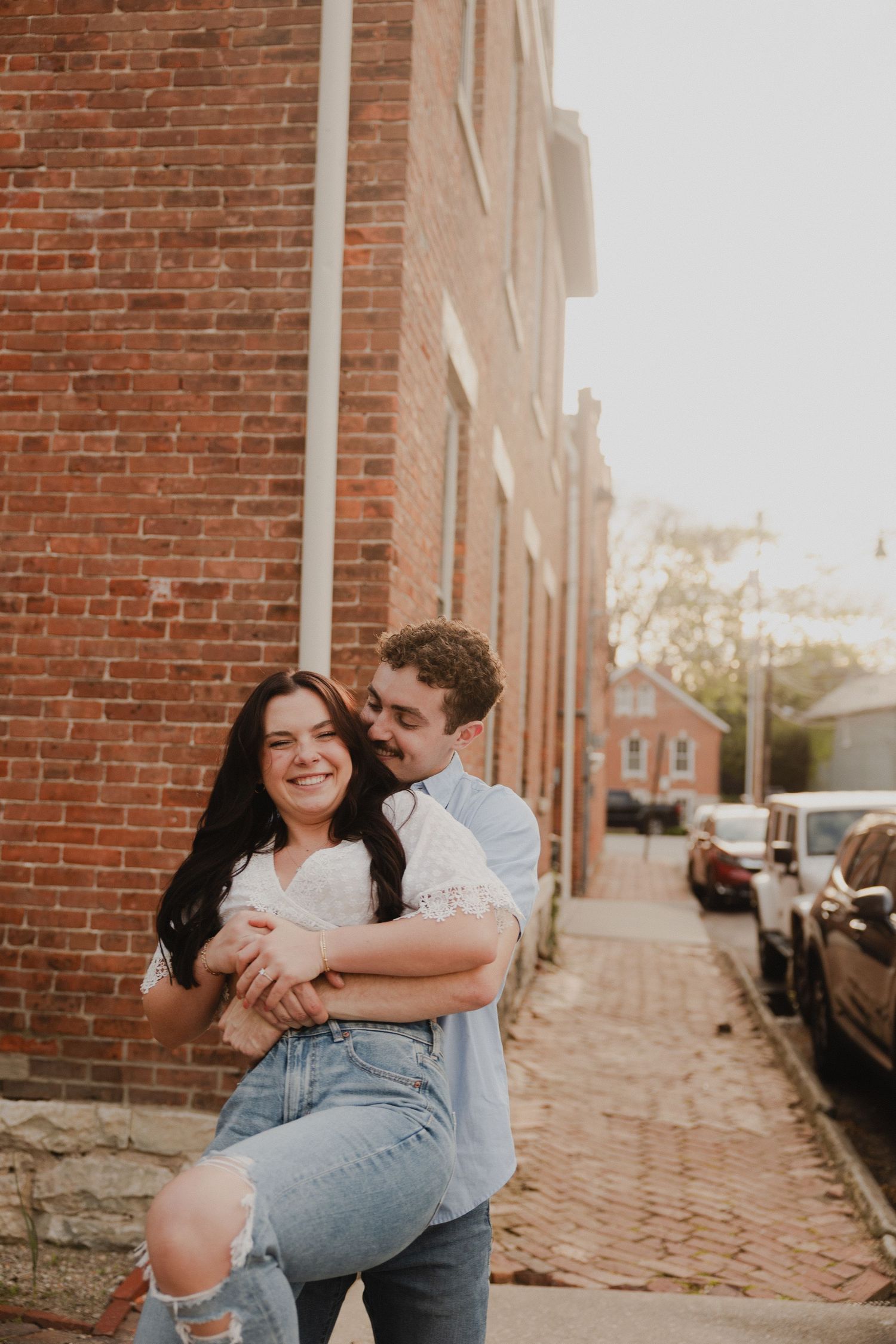 Couple shares playful moment on brick sidewalk in urban setting.