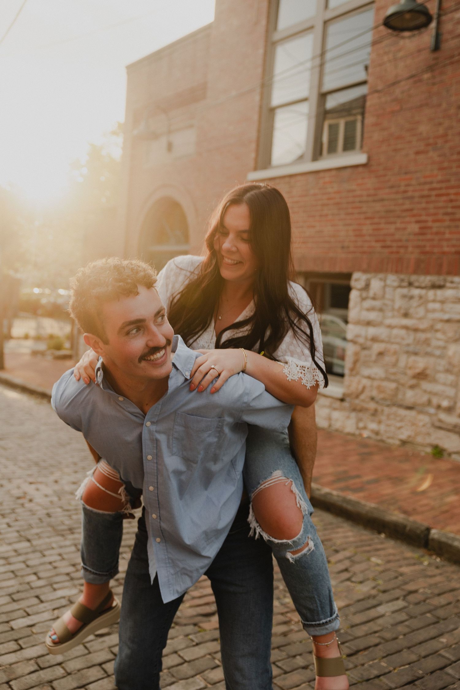Playful piggyback ride moment at sunset against brick building.