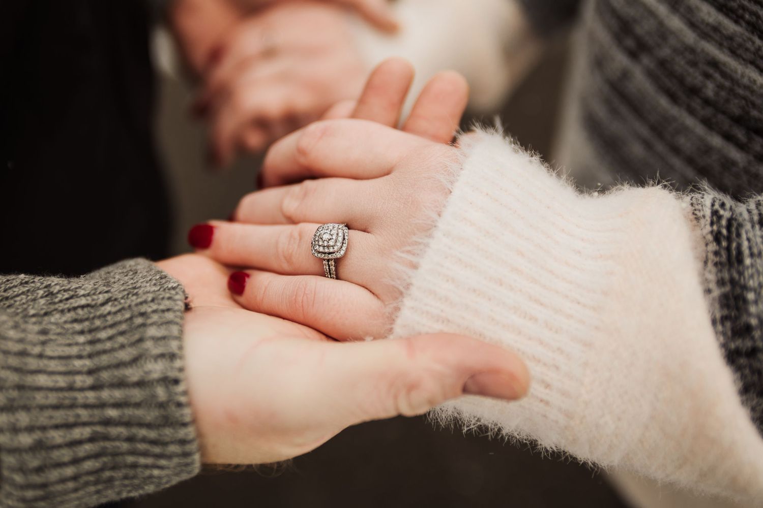 Close-up of hands showing off an engagement ring with a white sweater sleeve.