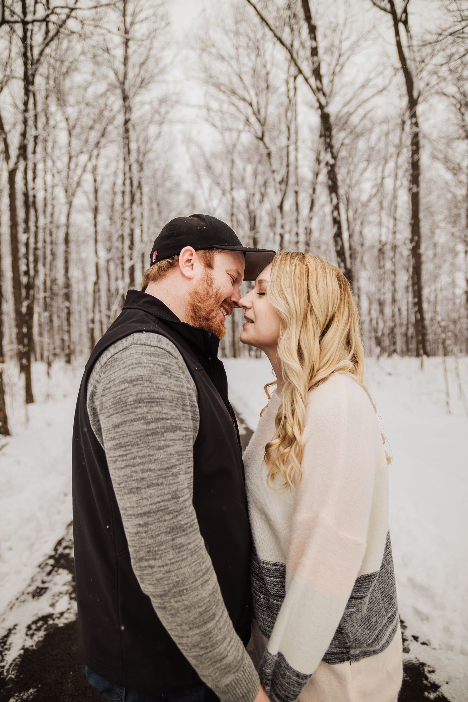 A couple shares a tender moment on a snowy forest path during their winter photoshoot.