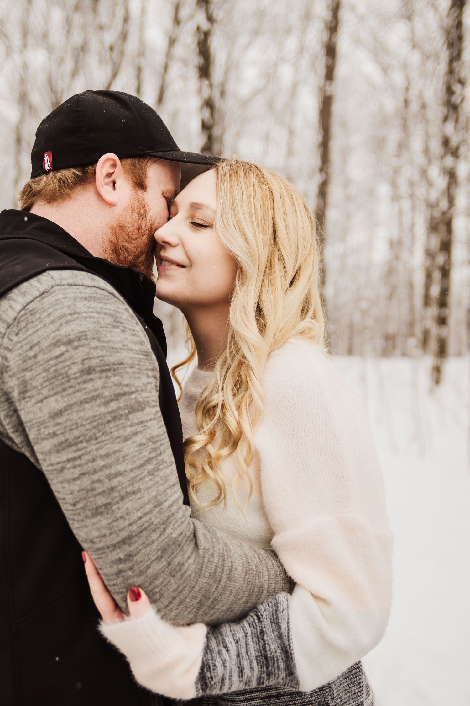 Intimate winter portrait of a couple embracing in a snowy forest setting.