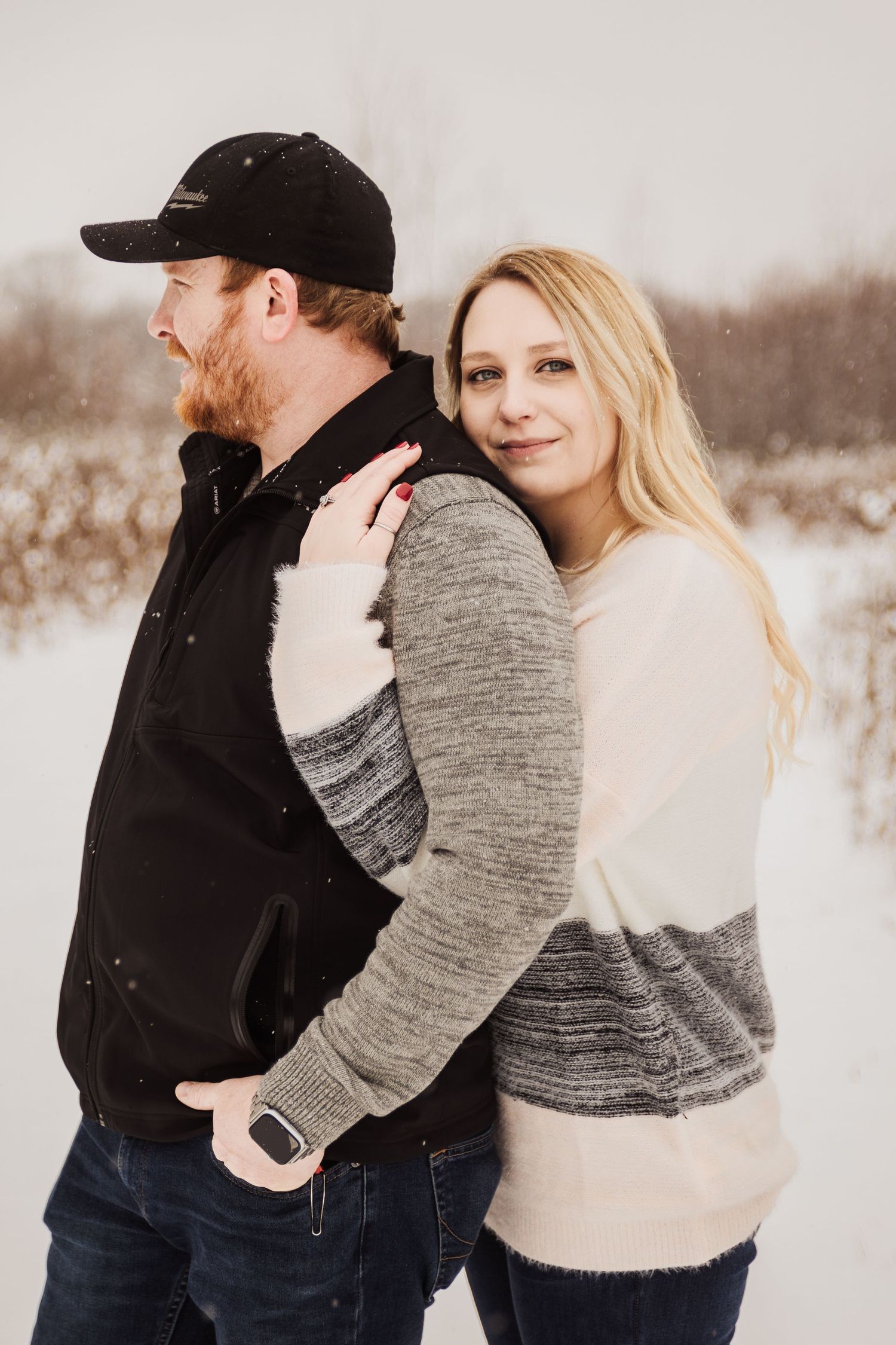 Couple in cozy winter sweaters posing together in a snowy field.