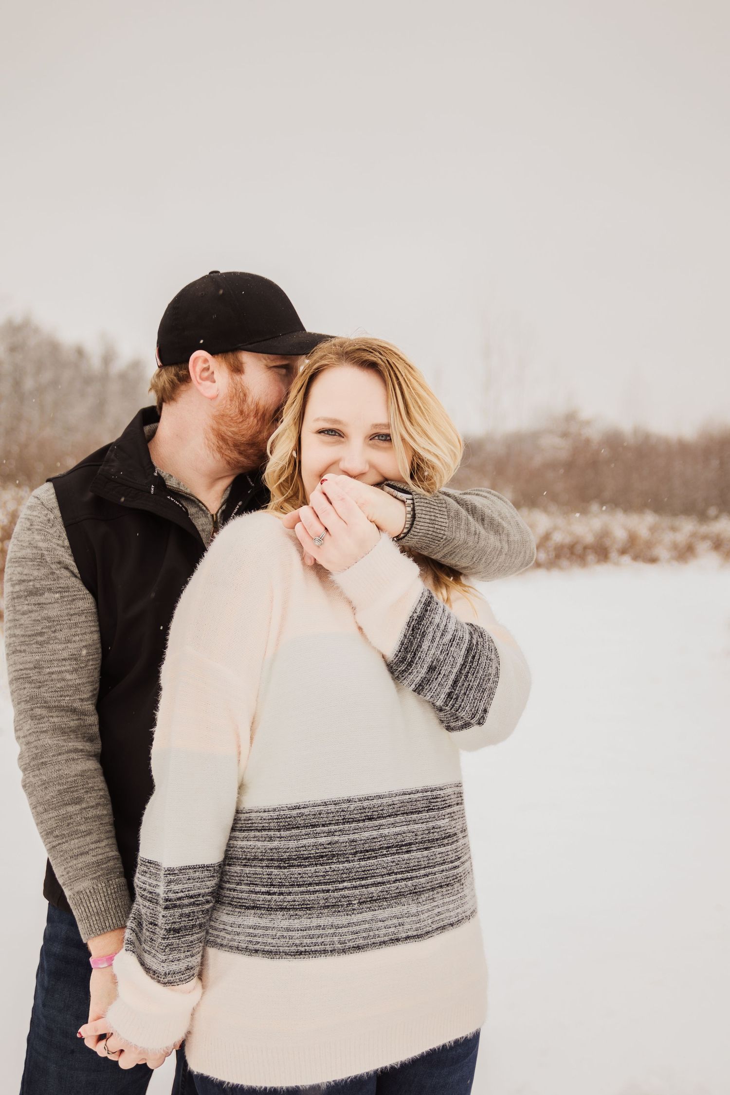 A candid winter engagement photo capturing a joyful laughing moment between a couple.