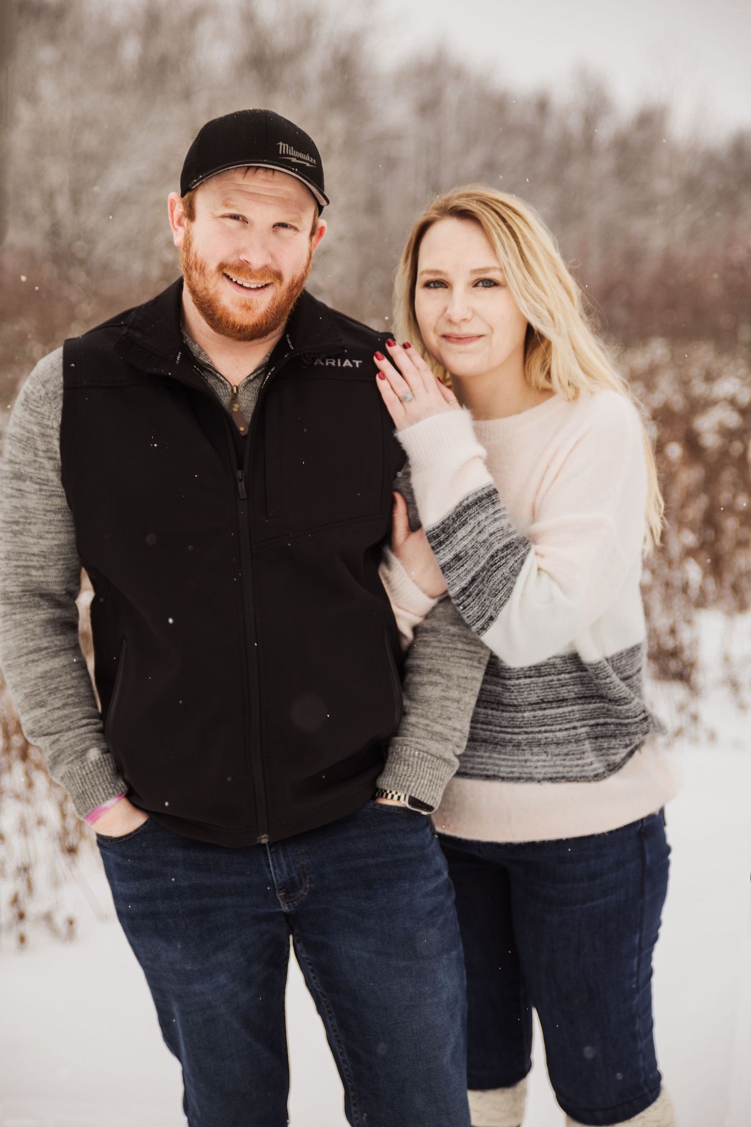 A happy couple poses for their winter engagement photos wearing coordinating sweaters in the snow.