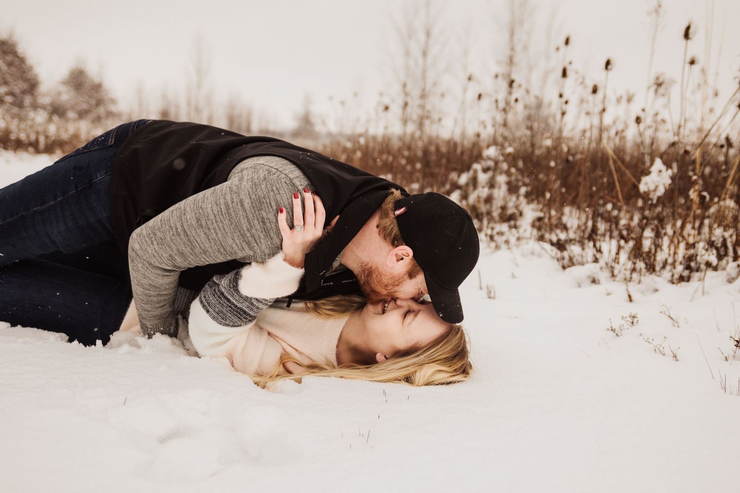 A couple shares an intimate moment lying in the snow during their winter photo session.