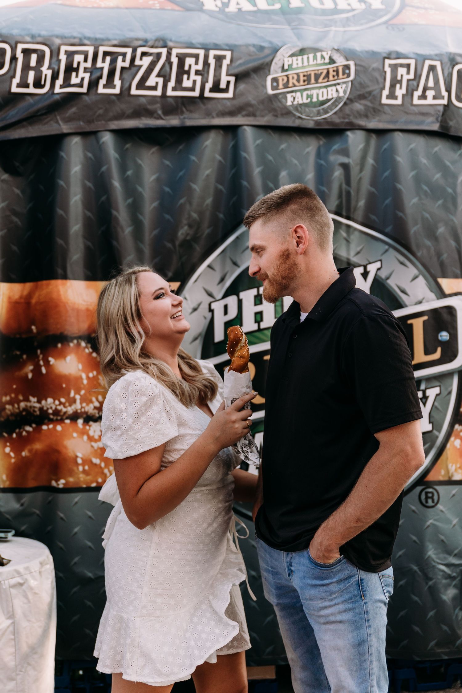 A couple sharing a laugh in front of a Pretzel Factory banner.