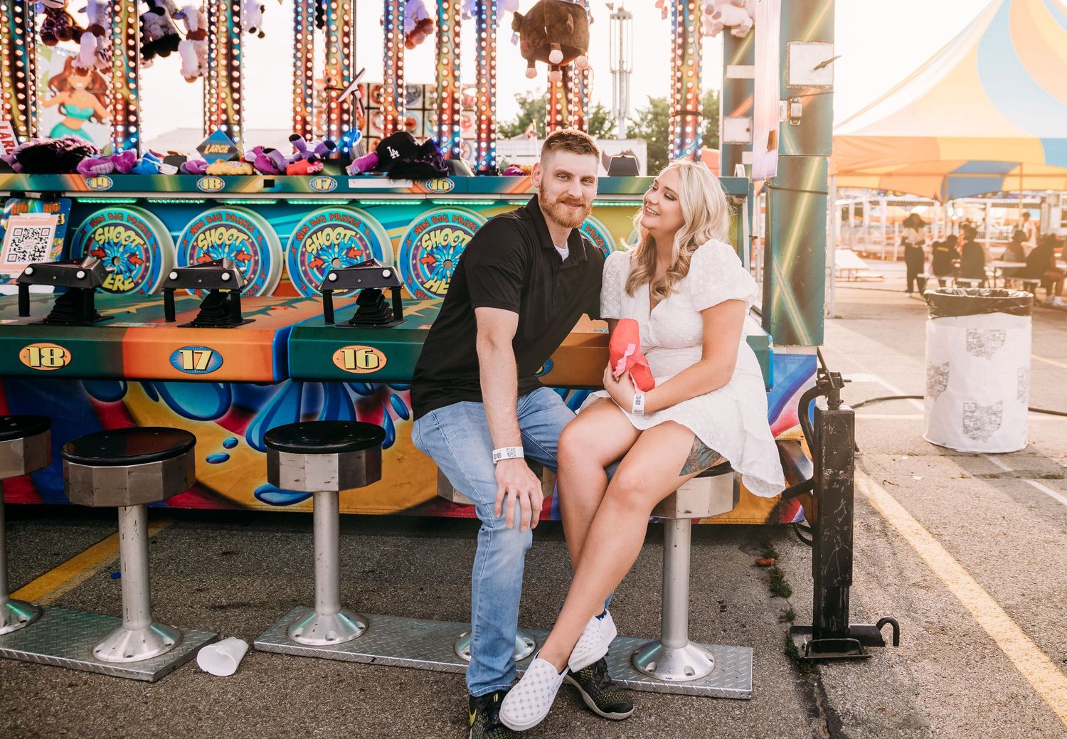 A couple relaxes on carnival ride seats surrounded by festive lights and decorations.