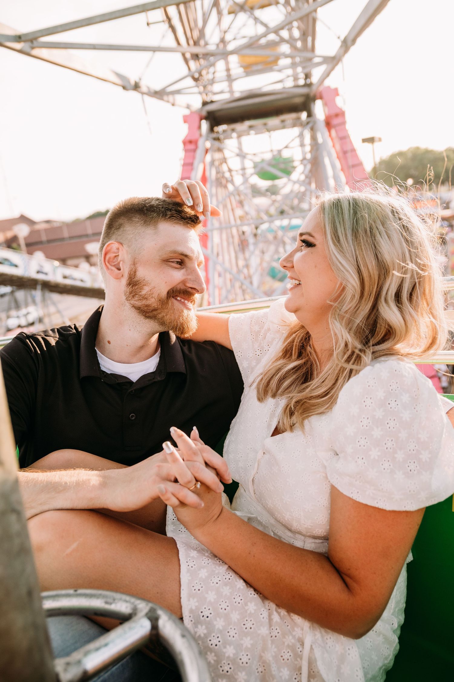 A couple shares a joyful moment on a carnival ride with ferris wheel in background.