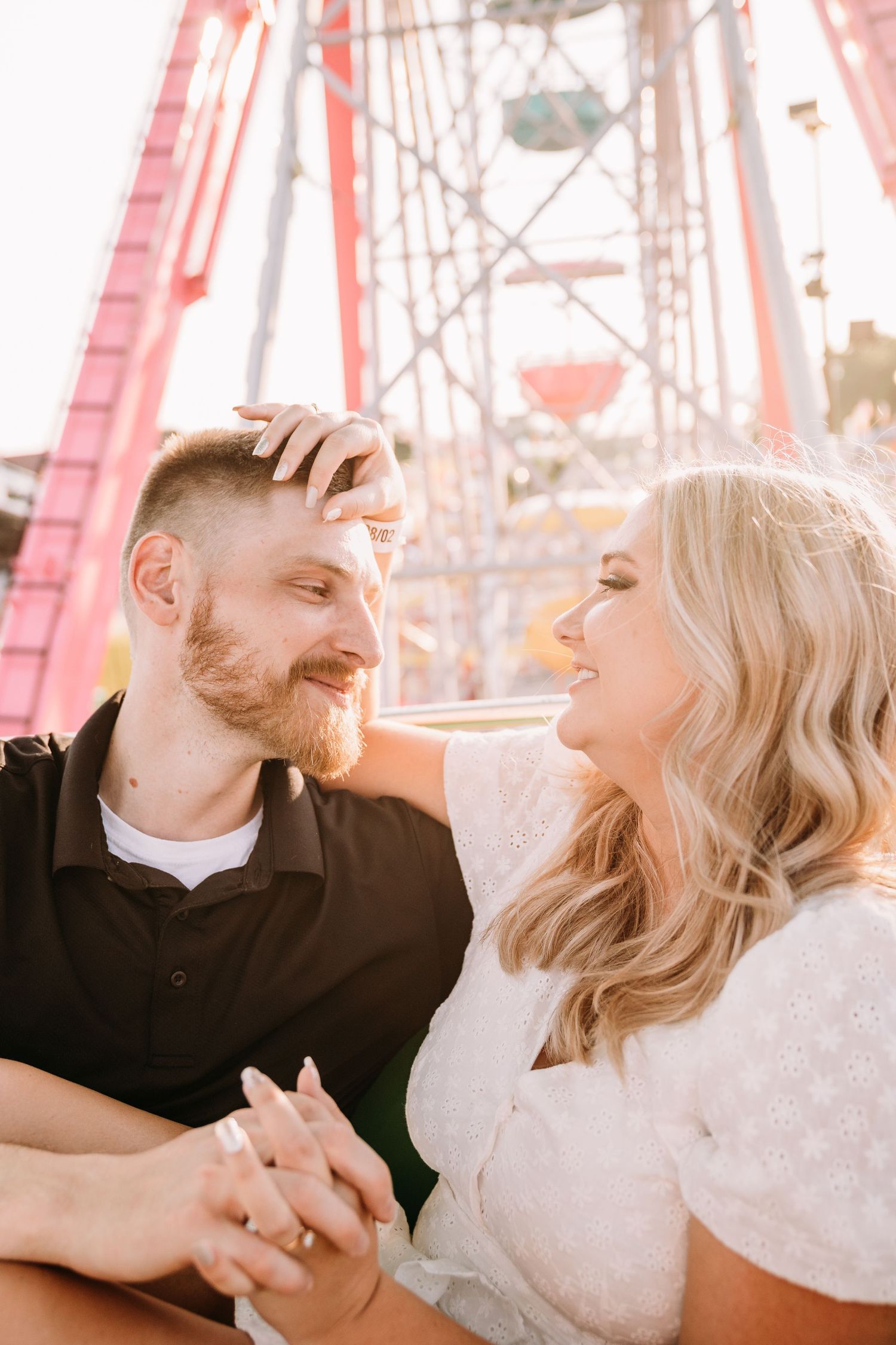 A couple gazes at each other while sitting at a carnival with rides visible behind them.