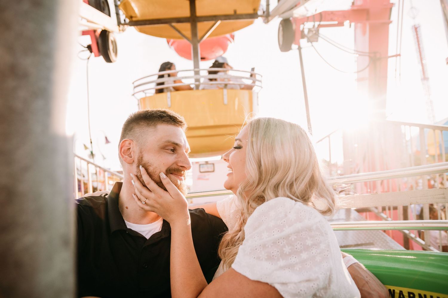 A playful couple shares a moment on a carnival ride with sunset lighting.