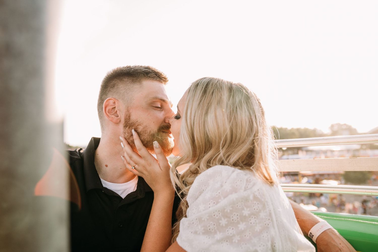 A romantic couple shares an intimate kiss at sunset on a carnival ride.