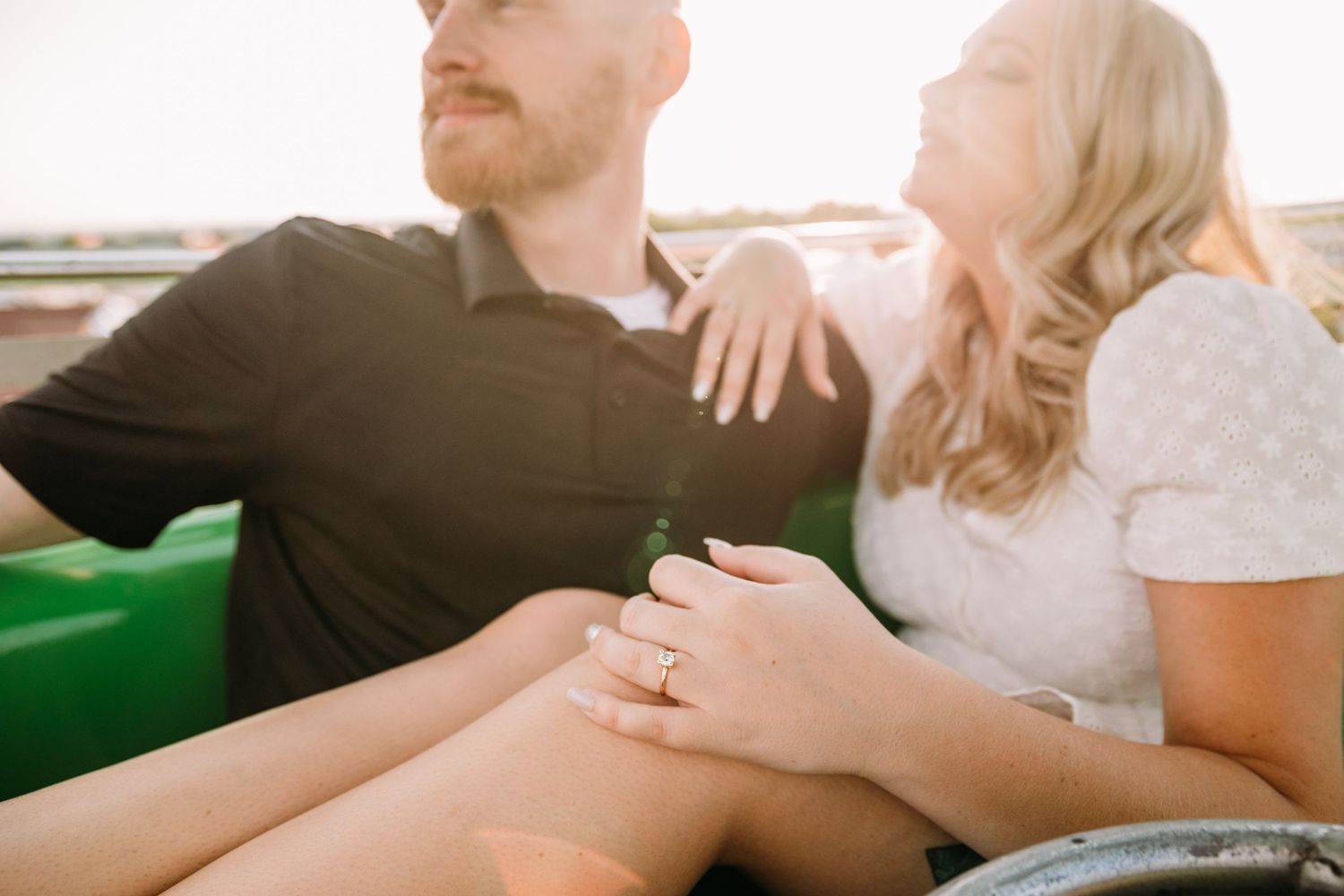 A couple in casual attire sits close together showing off an engagement ring.