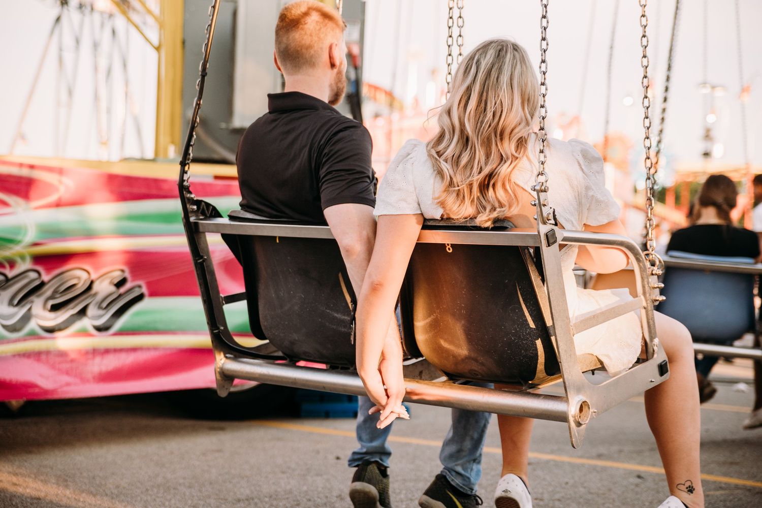 A couple sitting together on carnival swings during sunset.