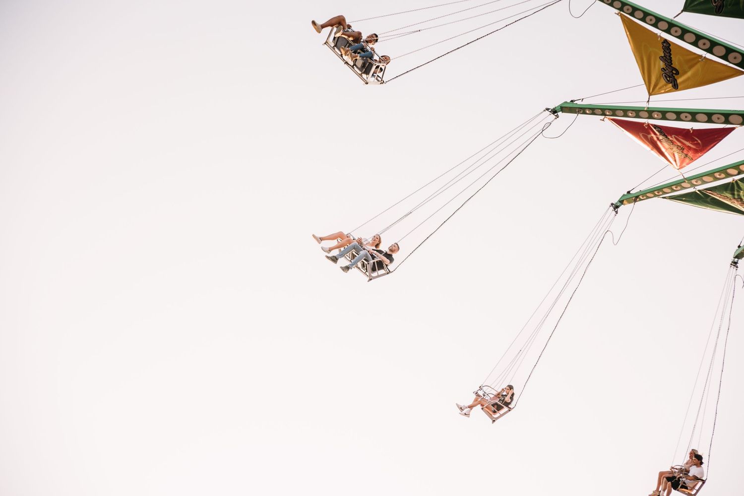 Multiple swing ride seats silhouetted against a bright sky at an amusement park.