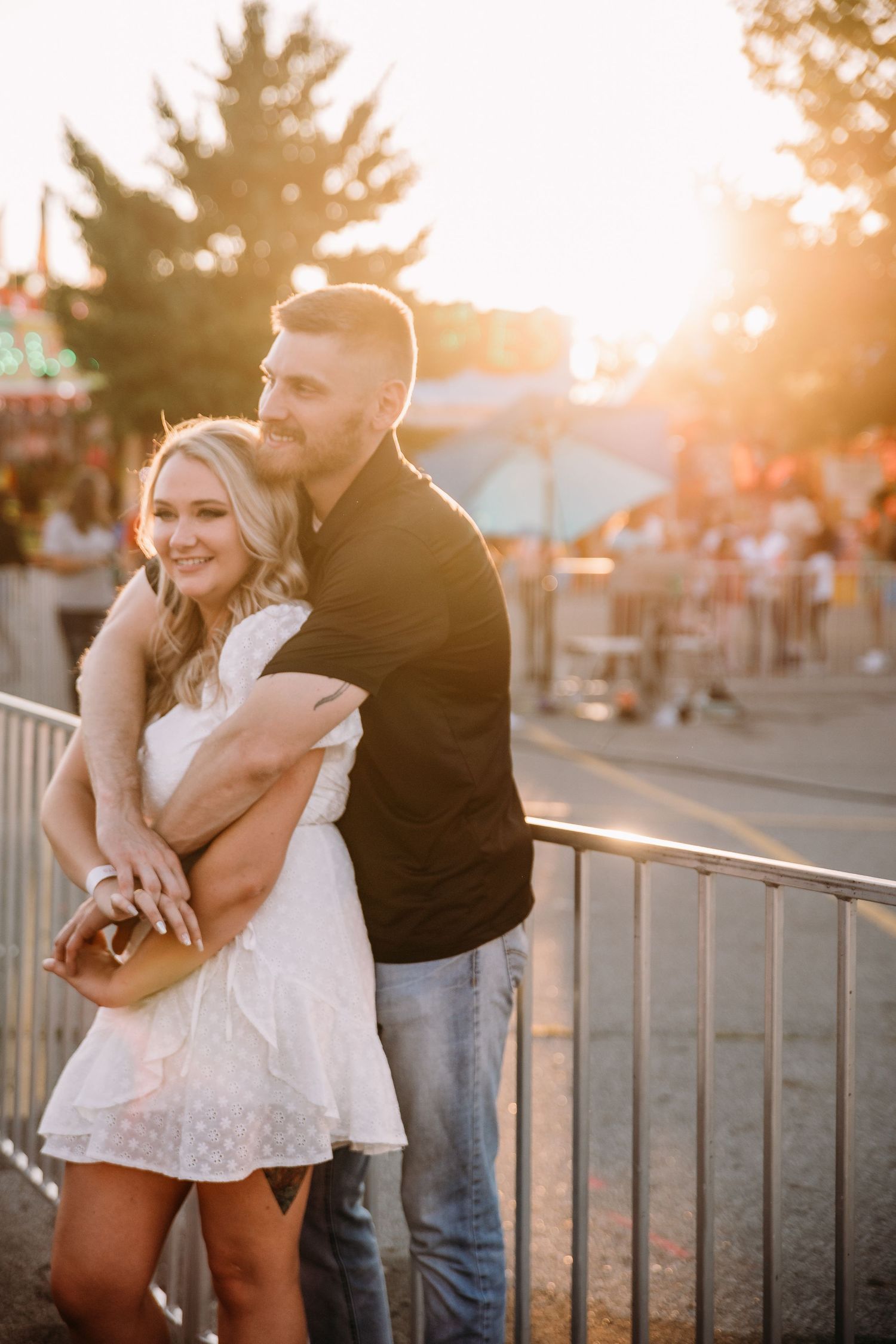 A couple shares an intimate moment against carnival railings at golden hour.