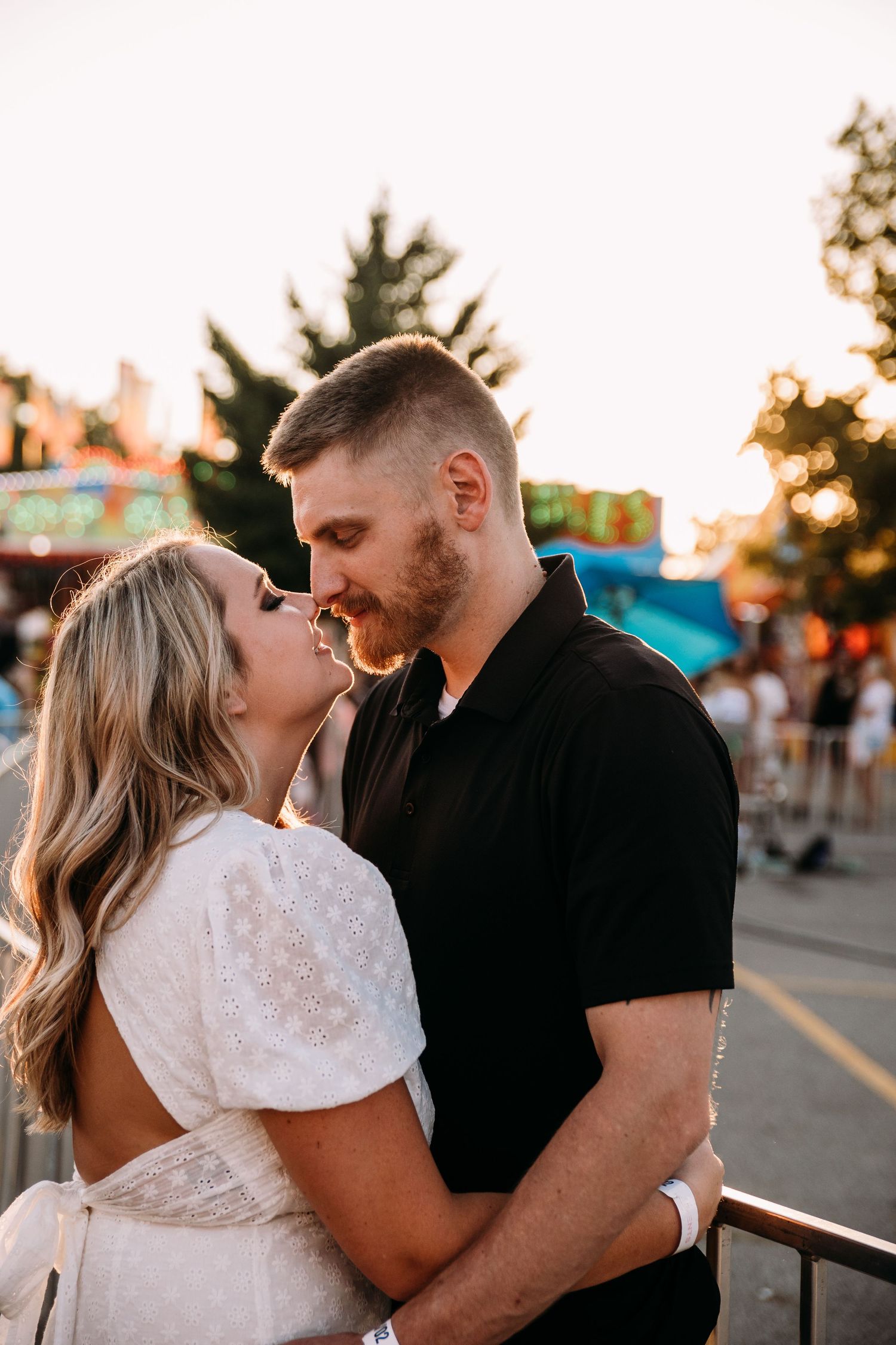 A romantic moment between couple in white dress and black polo at sunset carnival.