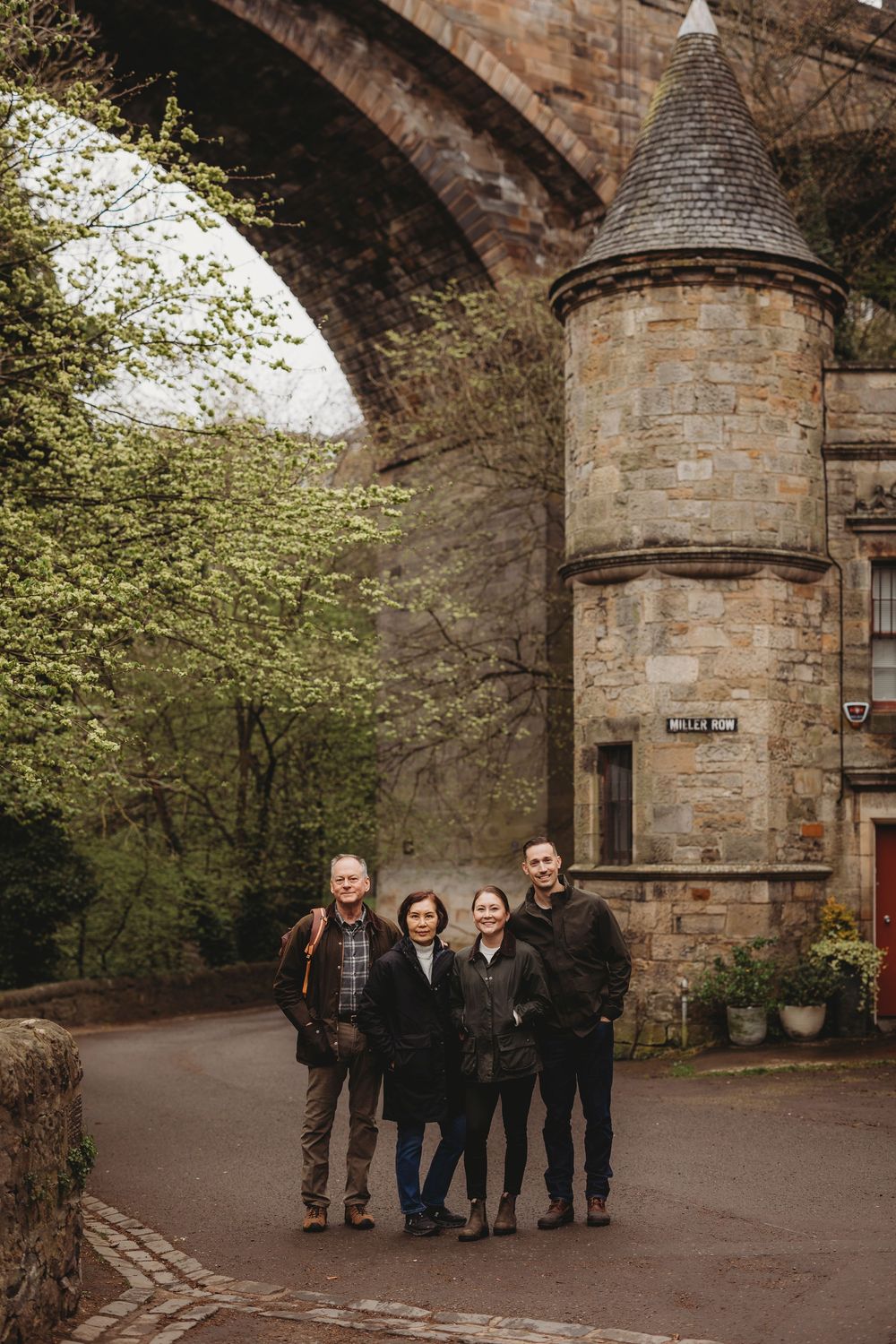 A stone castle entrance with a circular turret and archway surrounded by trees in a scenic outdoor setting.