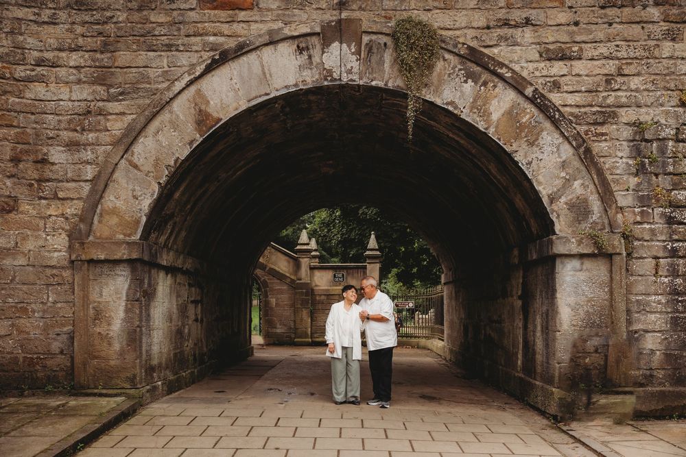 A couple poses together under a rustic stone archway tunnel in matching white outfits.