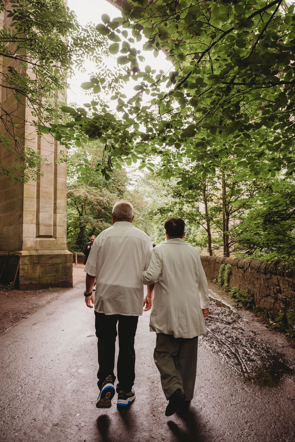 Two individuals stroll together along a tranquil tree-lined path on an overcast day.