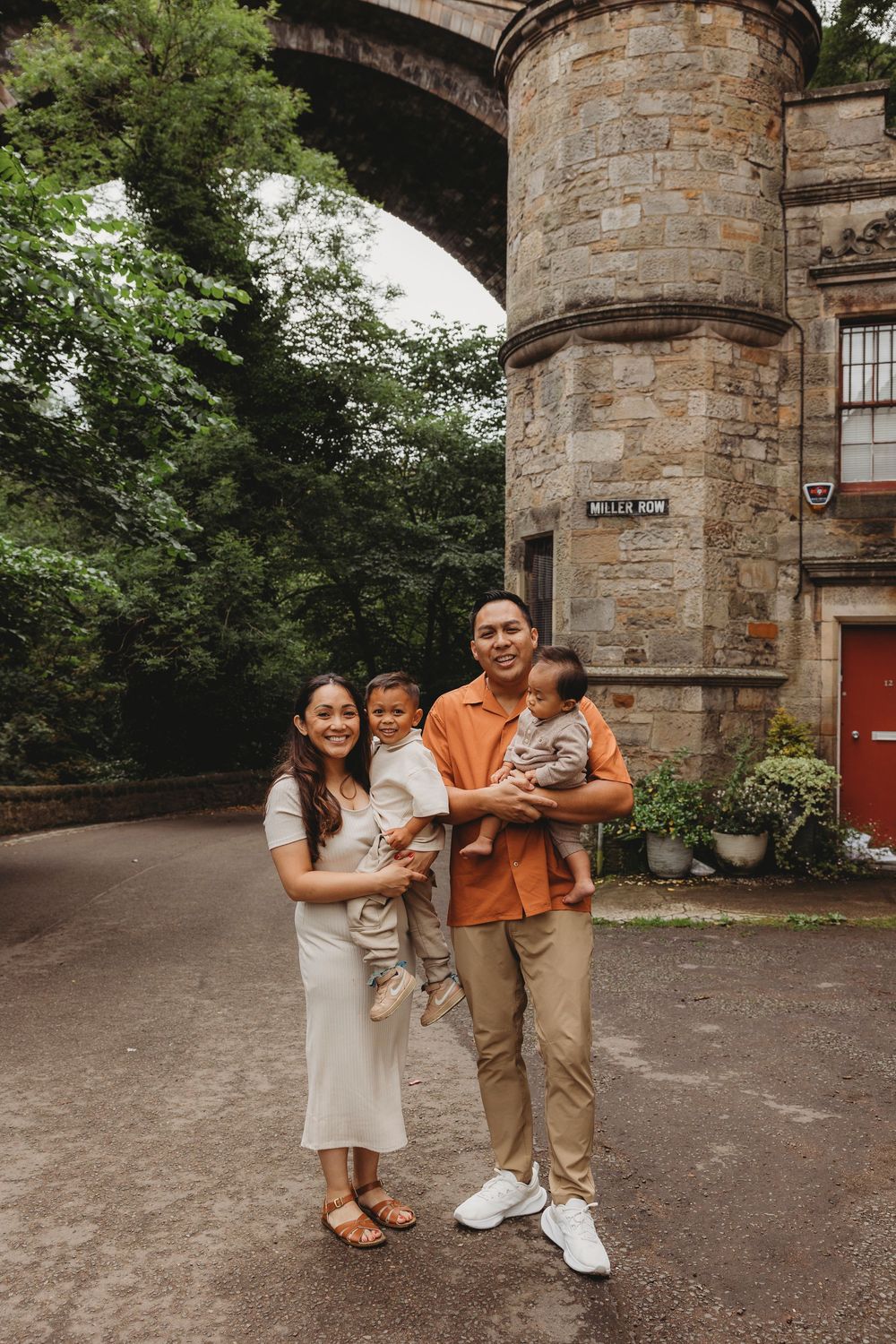 A family of four poses together in front of a historic stone tower and archway.