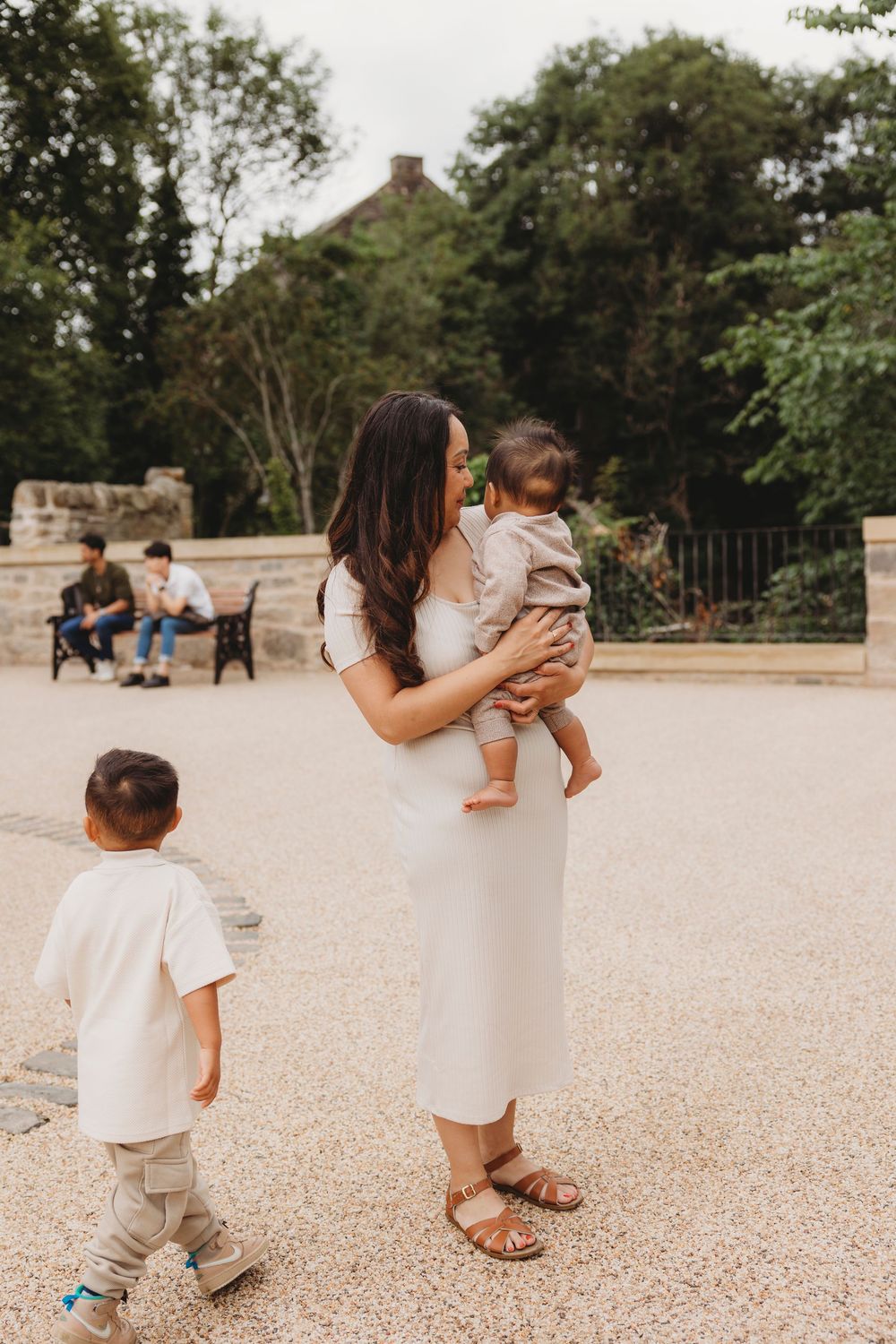 Family enjoying a peaceful afternoon walk in a park with stone benches and lush greenery in the background.