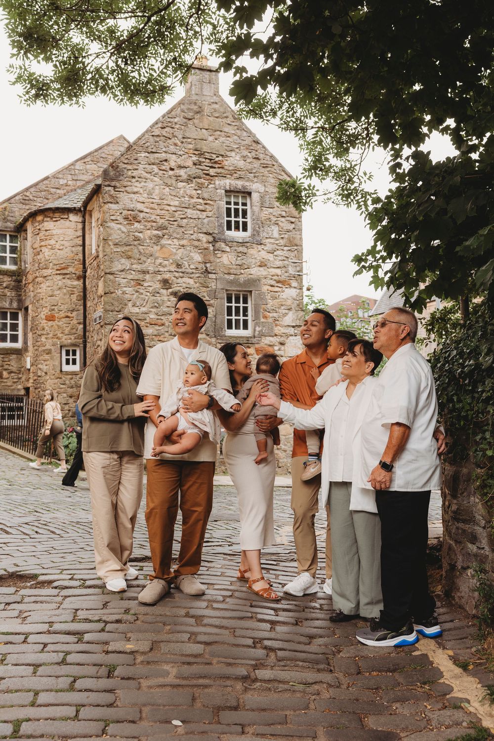 Multi-generational family gathers on a cobblestone street in front of rustic stone building in warm lighting.