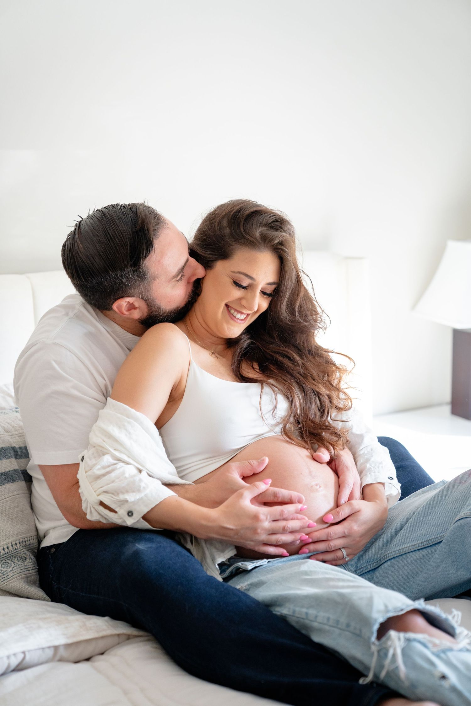 A couple embraces tenderly on a bed as they share an intimate moment celebrating pregnancy together.