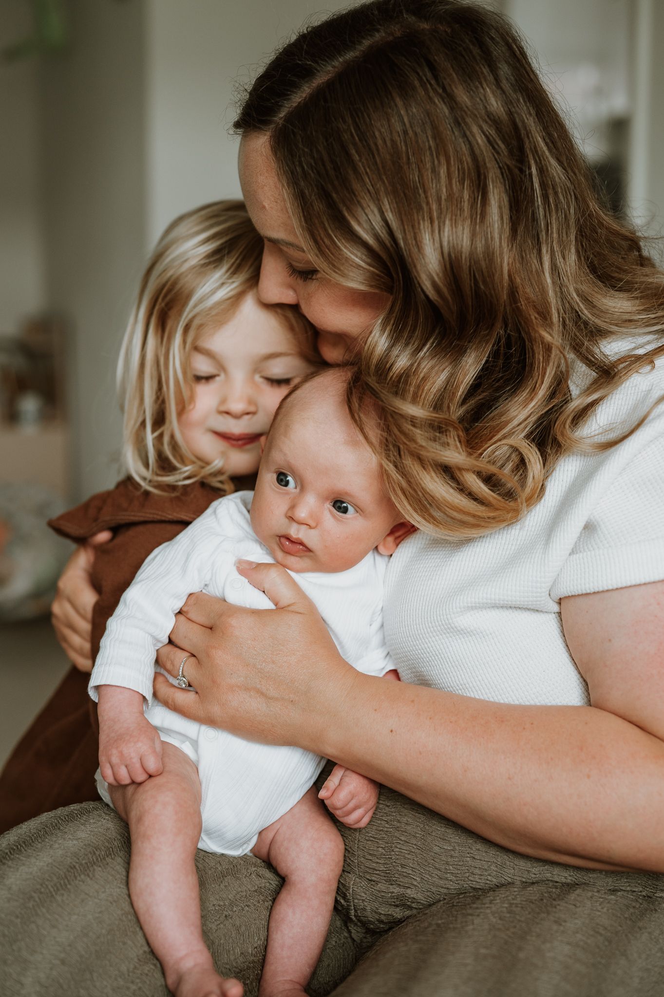 A tender moment shared between siblings and parent cuddling together in soft natural lighting at home.