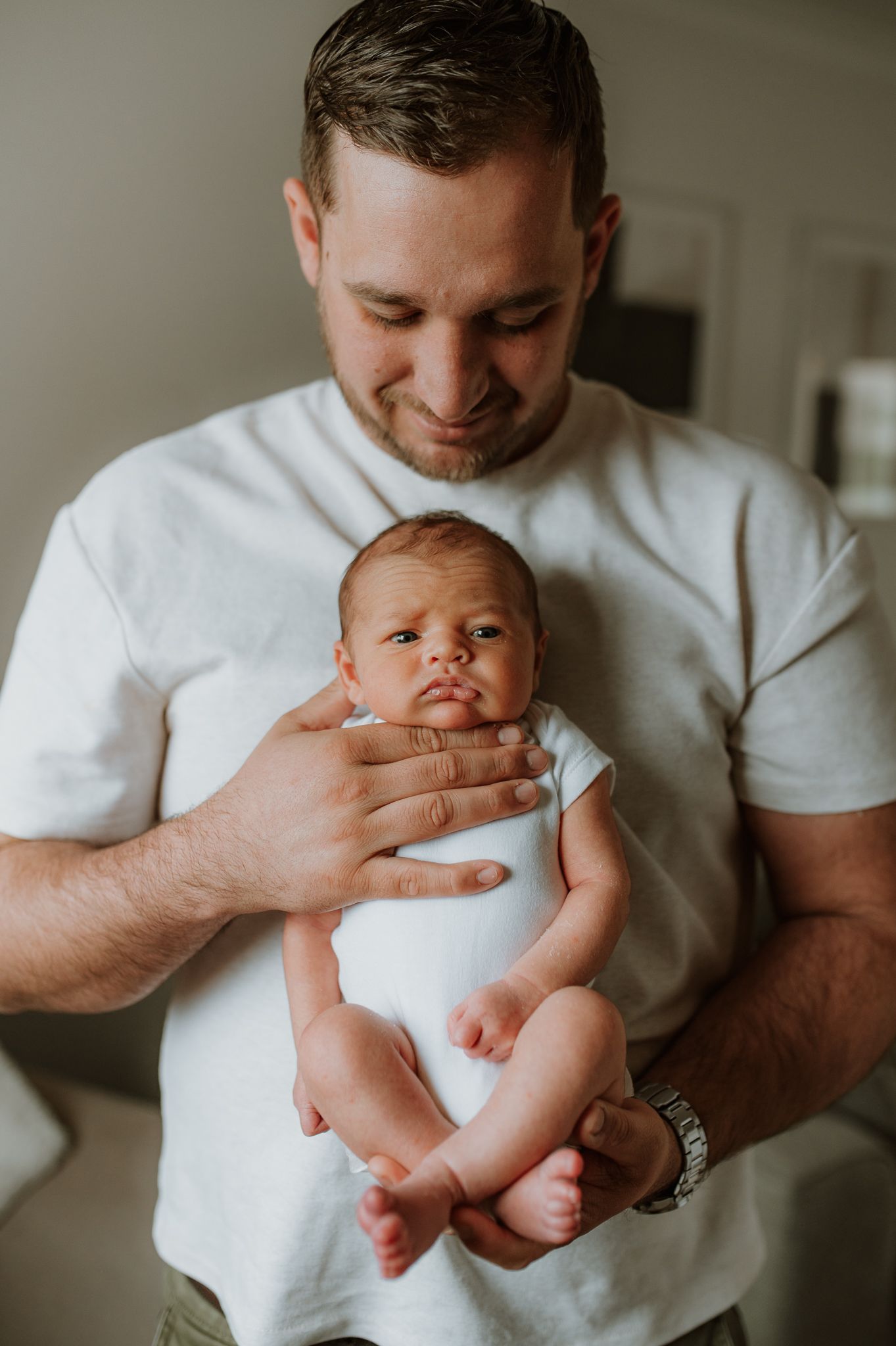 A tender moment captured as a parent in a white t-shirt gently cradles their newborn baby wearing a white onesie.
