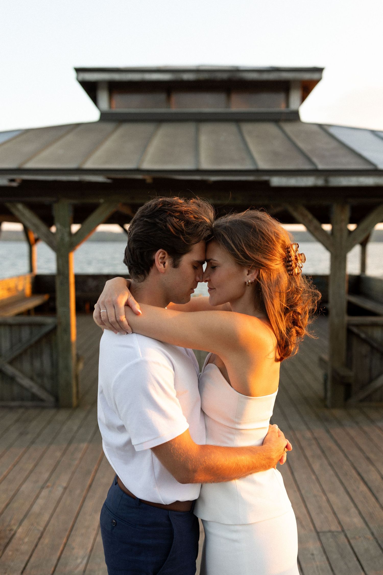 A sunset embrace on a wooden pier with a gazebo silhouetted in the golden hour light.