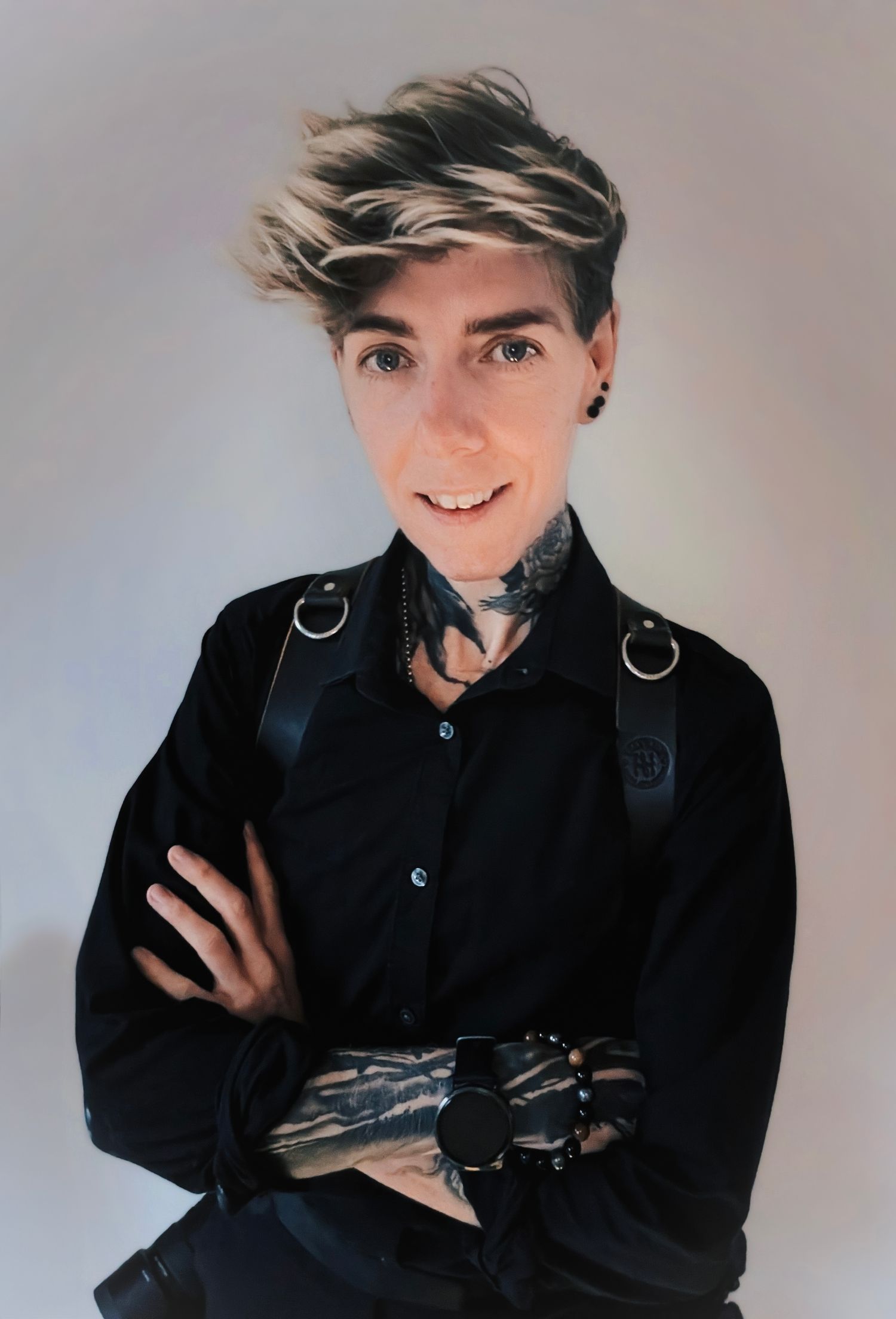Professional photographer in black attire with tattoos and a modern hairstyle.