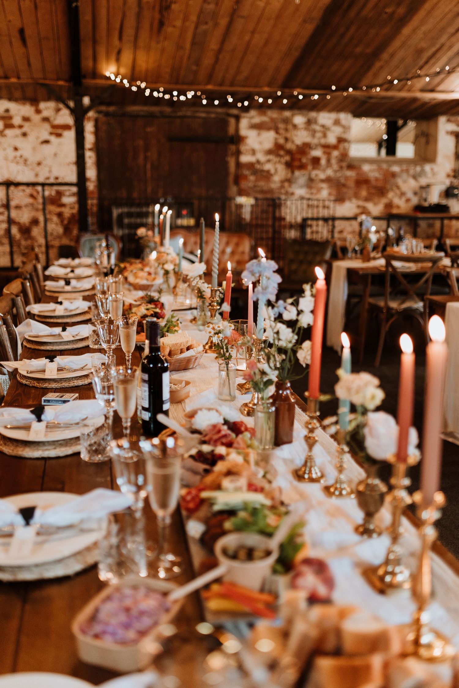 Rustic barn wedding reception table set with candles, string lights, and elegant place settings in warm ambient lighting.