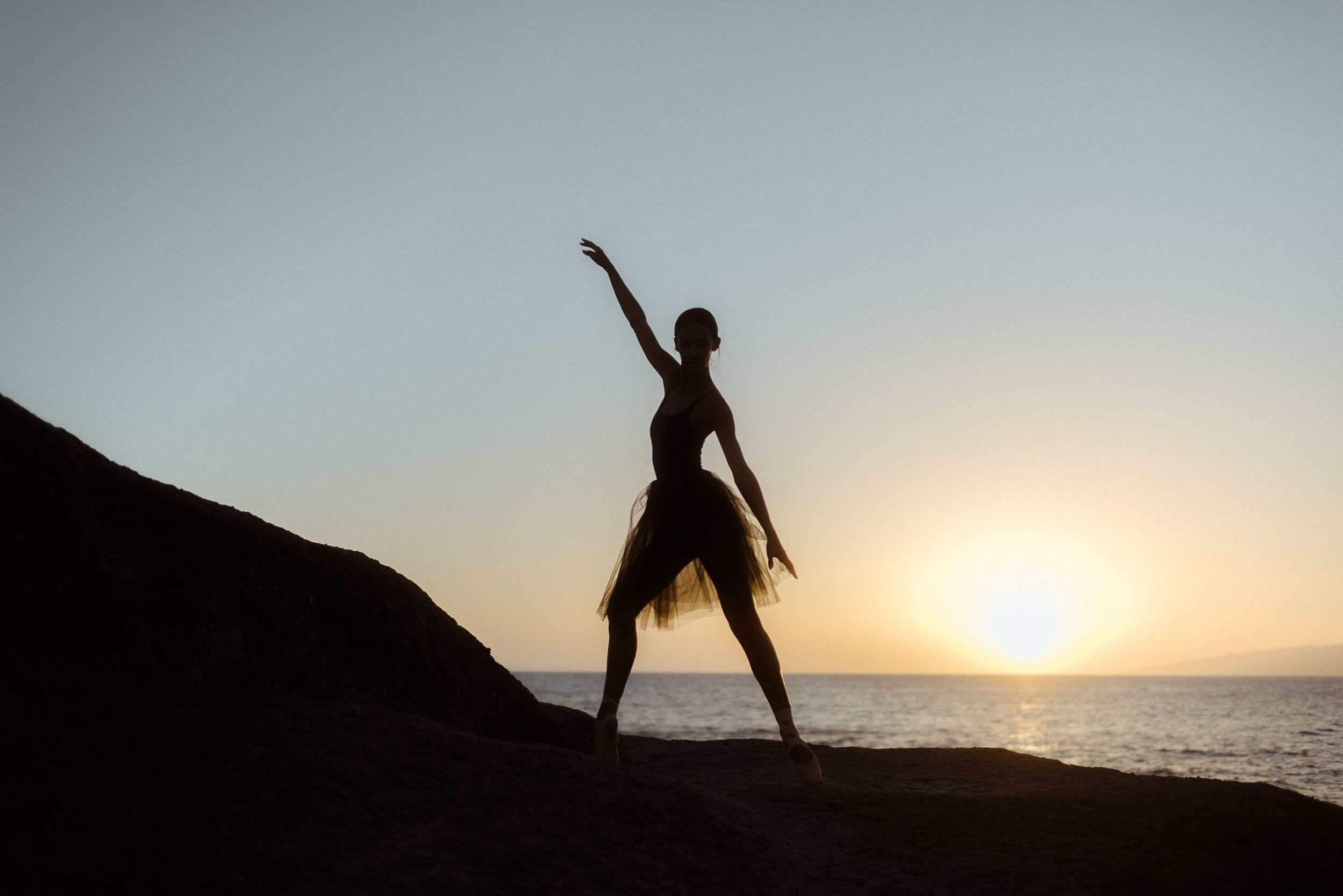 A dancer strikes a powerful pose at sunset on an oceanside cliff. Tenerife Wedding Photographer in La Caleta de Adeje.
