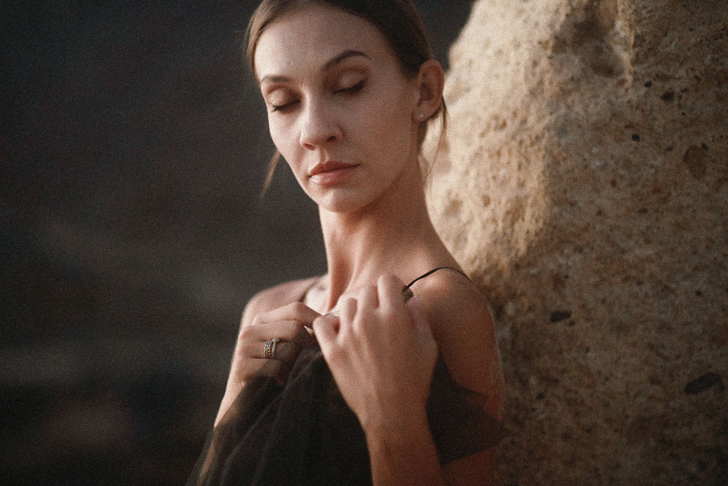 An artistic portrait of a dancer in black holding fabric against stone background. Tenerife Wedding Photographer in La Caleta de Adeje.