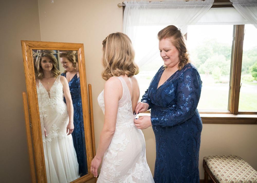 A touching moment as someone helps adjust a wedding dress in a room with a full-length mirror.
