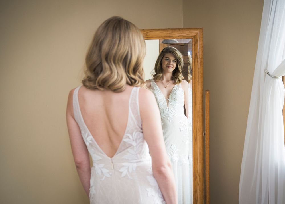 A bride in a white lace gown admires her reflection in a full-length mirror.
