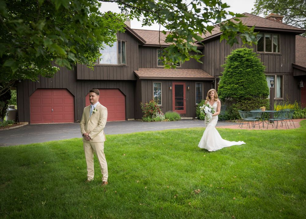 Wedding couple poses separately on lawn in front of a contemporary brown house with red garage doors.