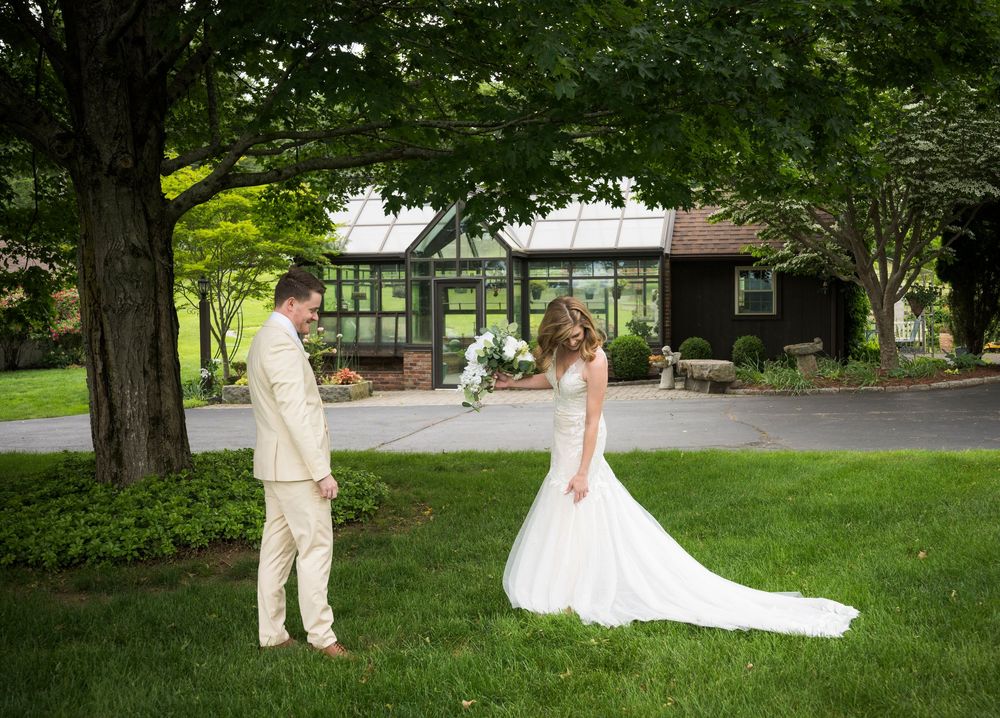 A couple shares their first look moment on a lush green lawn in front of a rustic venue.