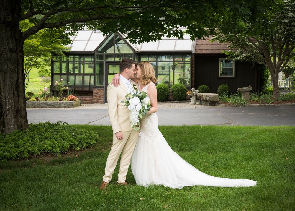 A romantic kiss between newlyweds on a manicured lawn with a Tudor-style building backdrop.