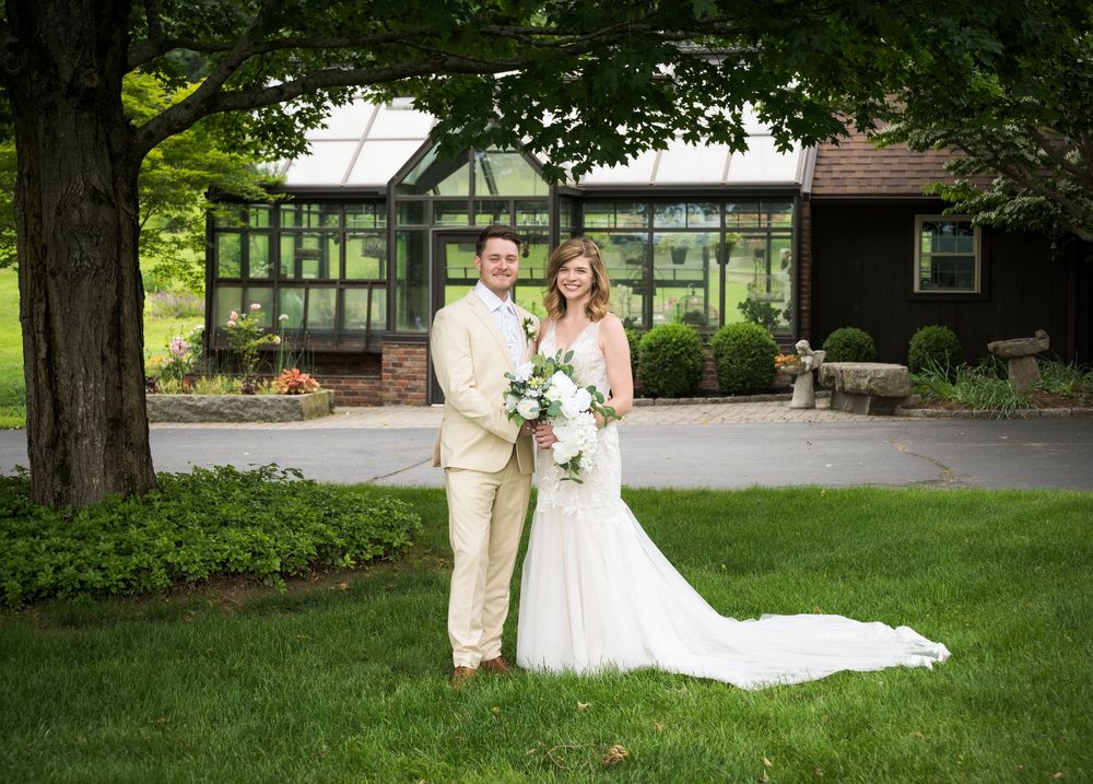 A newlywed couple poses for their wedding portrait in front of a rustic venue with beautiful landscaping.